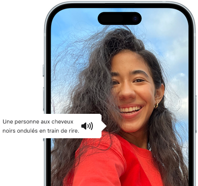 Ein iPhone 15 mit dem Feature VoiceOver, das eine Bildbeschreibung liefert: lachende Person mit welligem schwarzem Haar